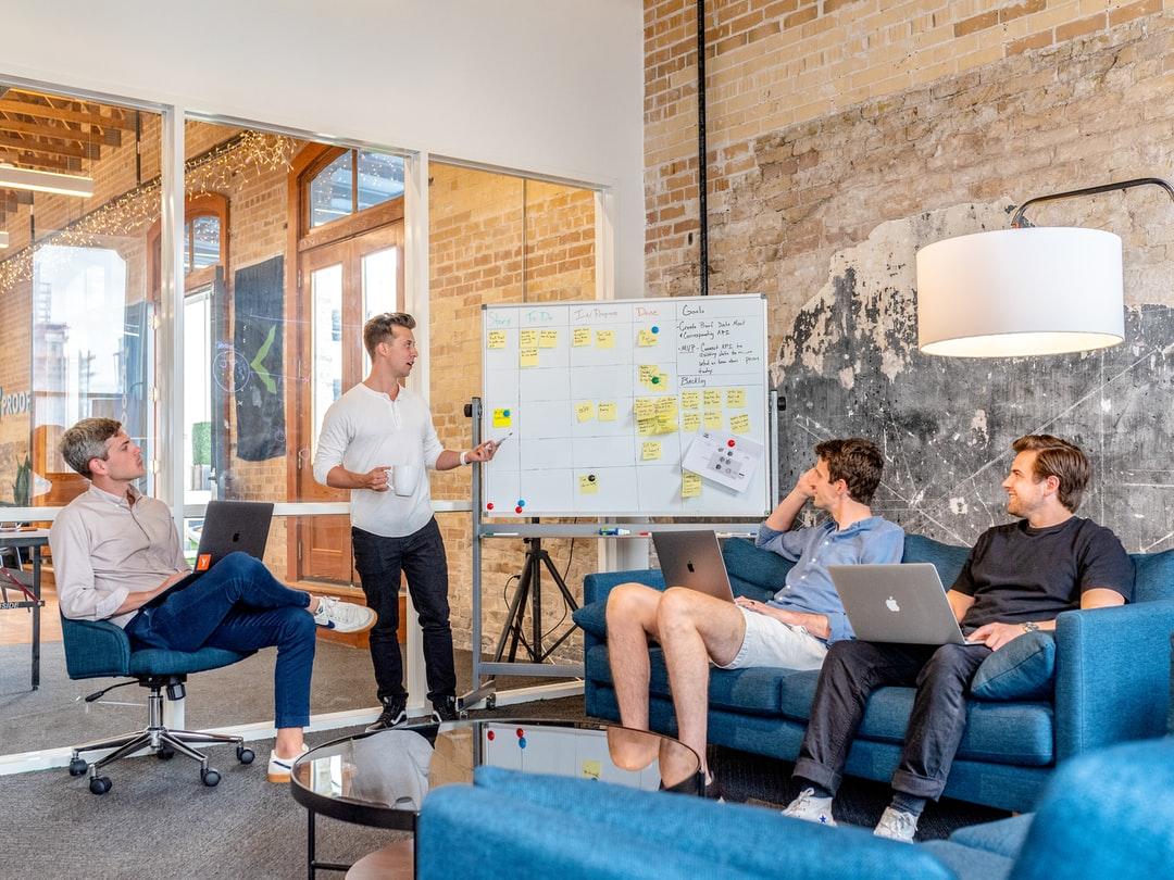 Team members in a meeting, looking at a board with sticky notes attached to it.