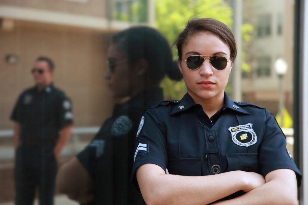 Female security guard wearing sunglasses standing in front of a reflective surface.