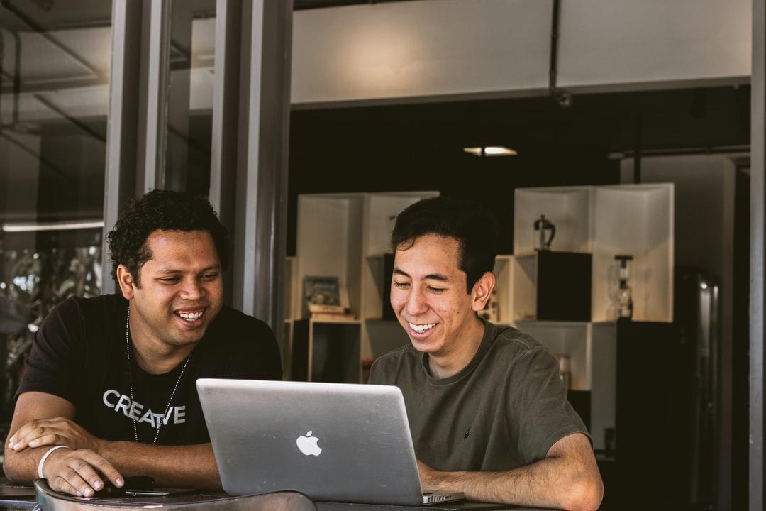 Two employees are meeting in front of a computer and smiling.